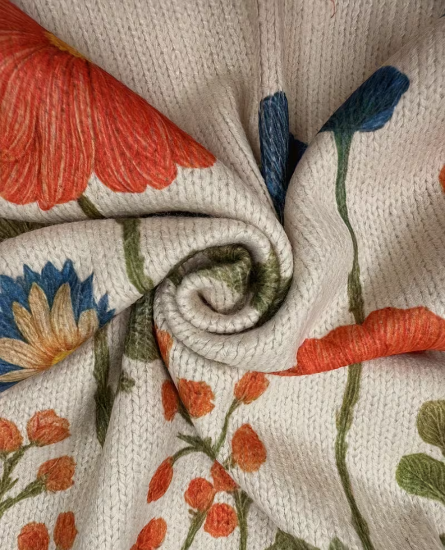 Floral knit cardigan close-up, cream texture with orange blossoms and blue stems
