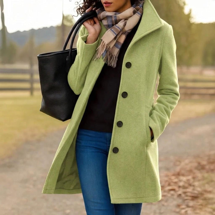 Light green long coat with dark buttons and notch lapels, worn over jeans with scarf