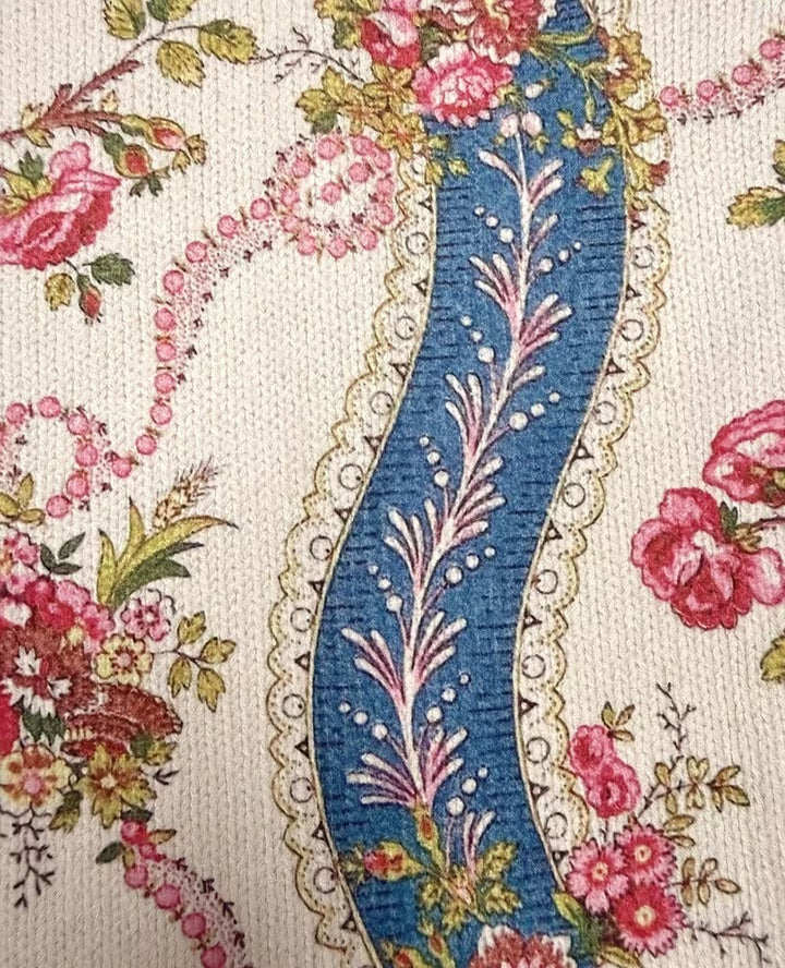 Close-up of cream knit fabric with blue floral motif and embroidered details